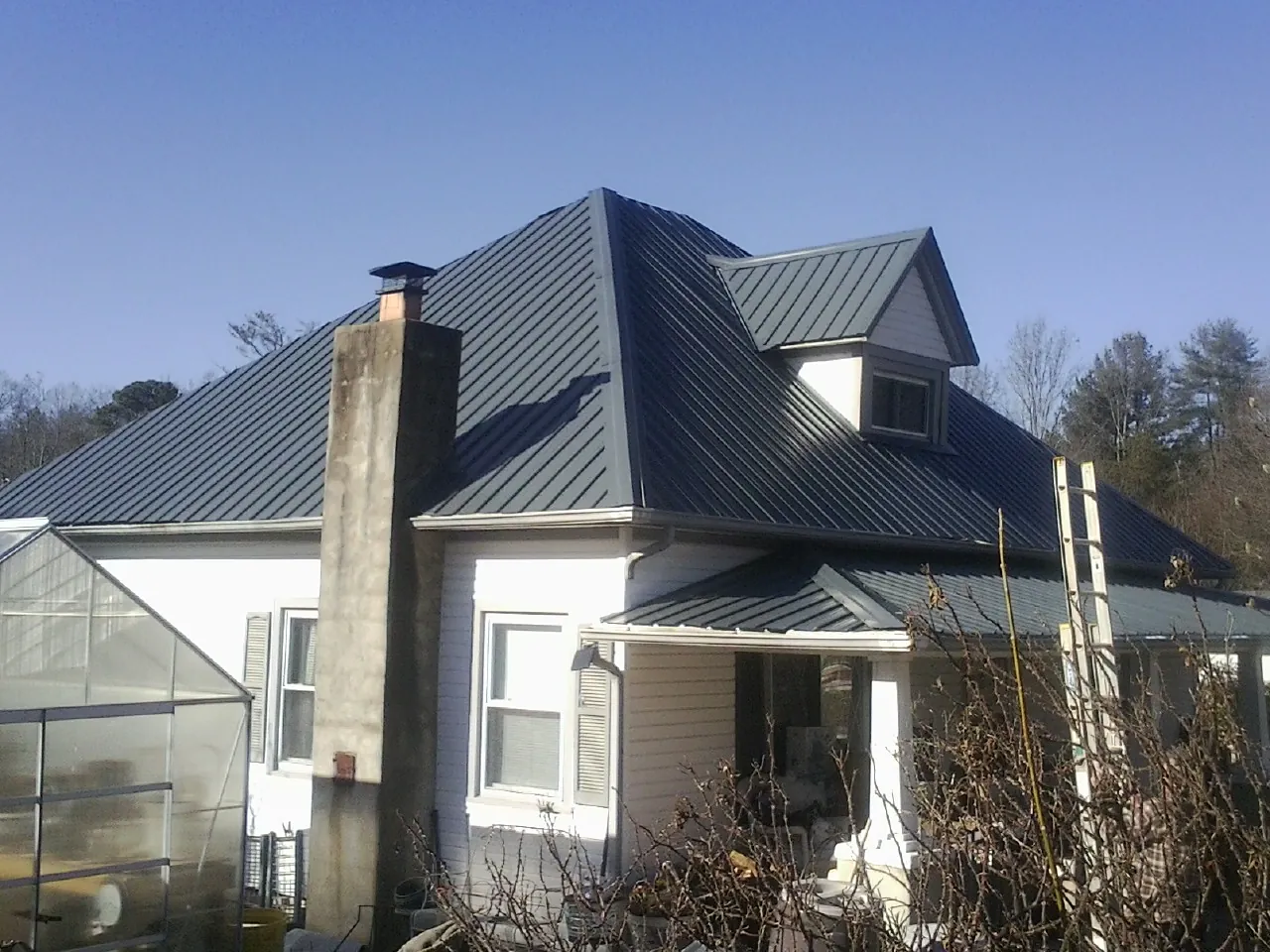Dark blue standing seam metal roof on a white farmhouse with dormer — Slate & Tile Roof Repair by Roofing Brothers in La Verkin