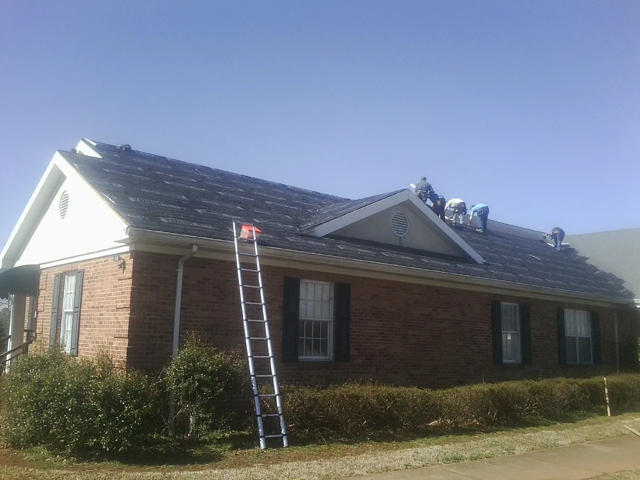 Crew tearing shingles off a brick ranch roof with a ladder set — Metal Roof Repair work by our crew in La Verkin