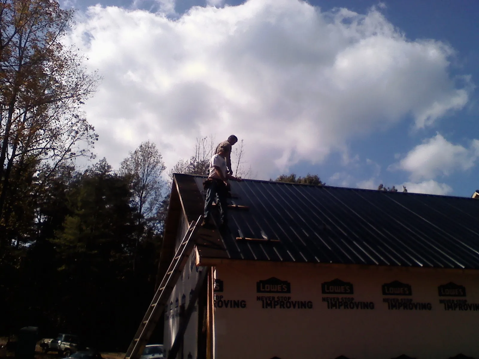 Roofer fastening dark metal panels high against a cloudy sky, from a Roof Inspection job in La Verkin