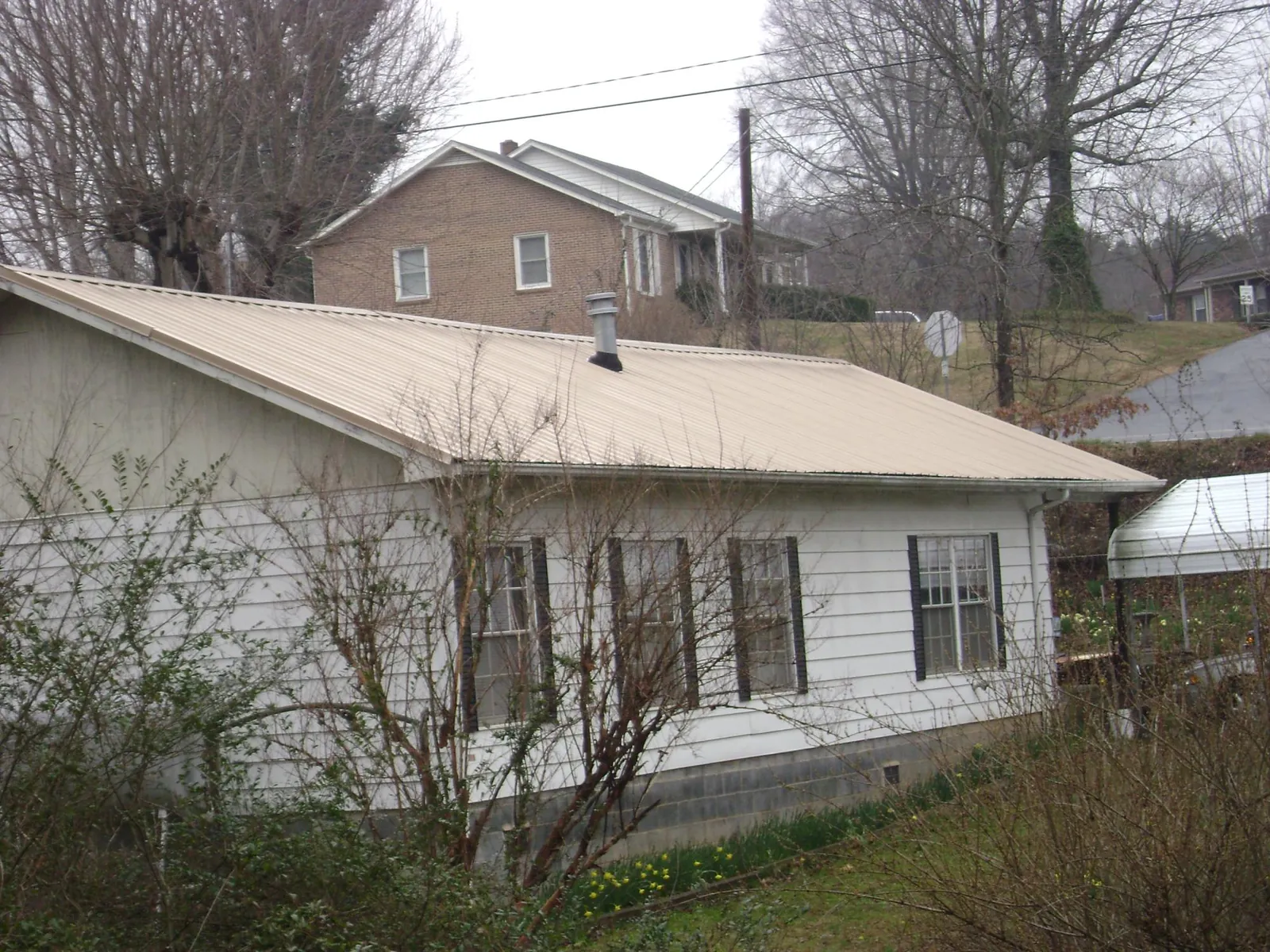 Tan metal roof on a white sided house set into a hillside — Commercial Roofing by Roofing Brothers in La Verkin